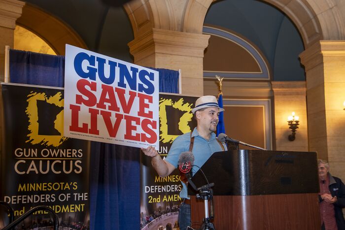 Man holding a guns save lives sign at a podium during a gun owners caucus event on gun laws in the U.S. debate