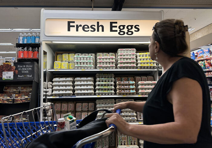 Woman with shopping cart looking at fresh eggs display in grocery store amid Trump gaslight claims on prime-time TV.