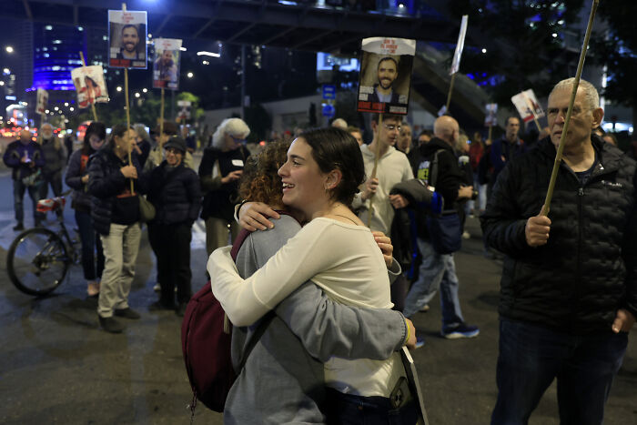 Protesters holding signs and two women hugging during a nighttime event that shook the world in 2025.