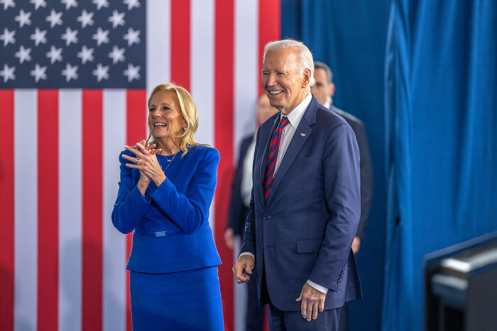 President Joe Biden and Jill Biden standing and smiling with an American flag backdrop during an event.