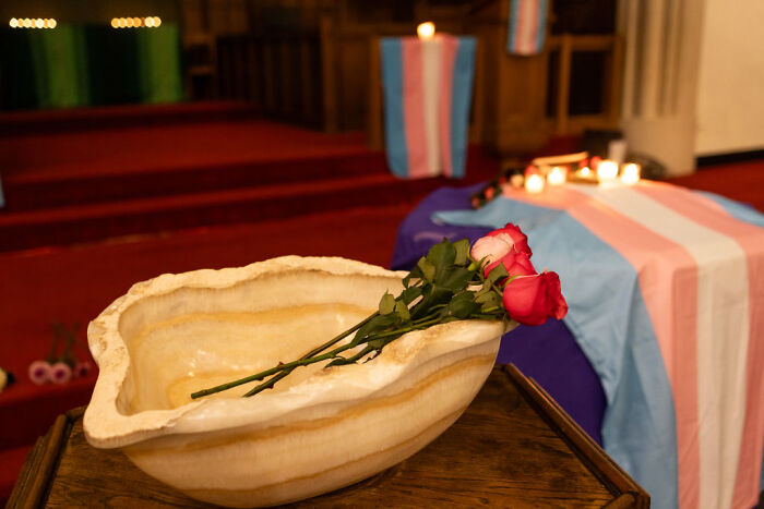 Memorial setup with roses and candles near a coffin draped in a transgender pride flag, symbolizing crimes that shocked the nation.