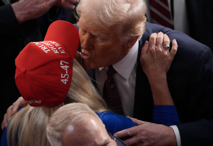 Former President Trump embracing a supporter wearing a red Trump hat amid Republican tensions and claims of secret mockery.