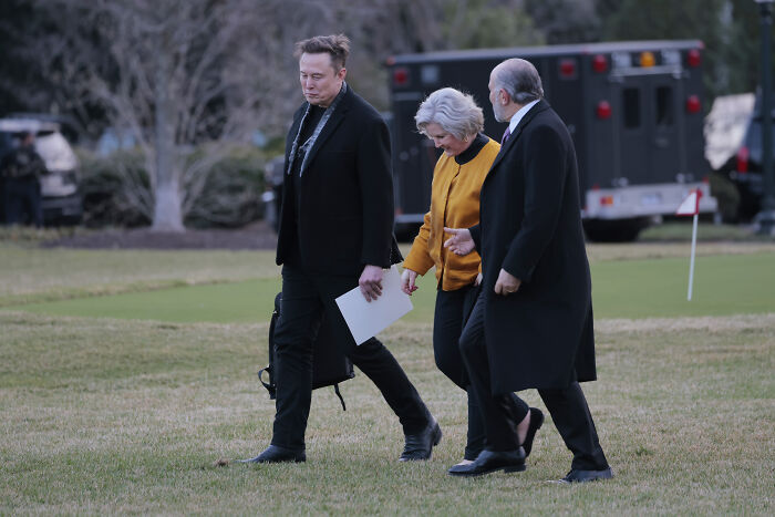 Three people walking outdoors near a golf green, illustrating Trump&rsquo;s chief of staff backpedaling after snitching claims.