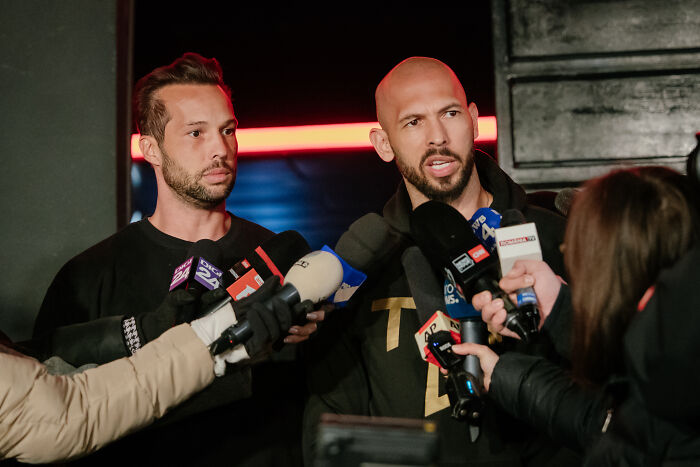 Two men speaking to reporters with microphones, addressing questions about misogynistic influencer allegations.
