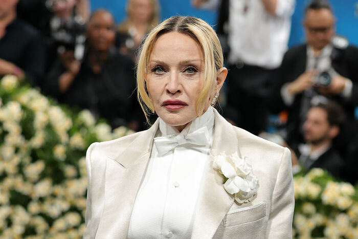 Madonna wearing a white suit with a flower at a public event, reacting to Trump administration&rsquo;s World AIDS Day decision.