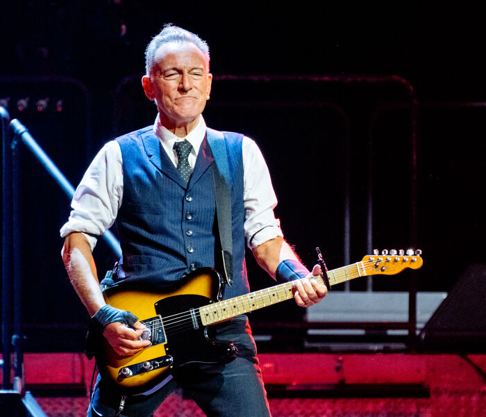 Male musician playing electric guitar on stage, representing celebrities who slammed Donald Trump in 2025.