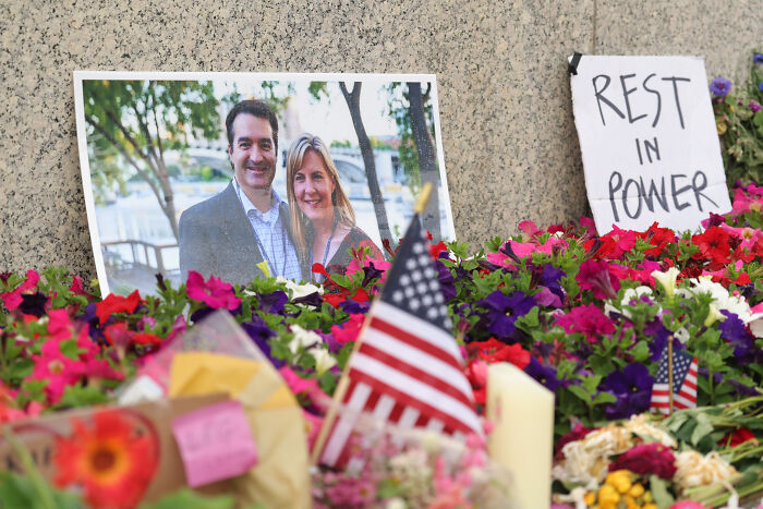 Memorial with a photo of a couple, American flags, flowers, and a sign saying REST IN POWER, related to shocking crimes.