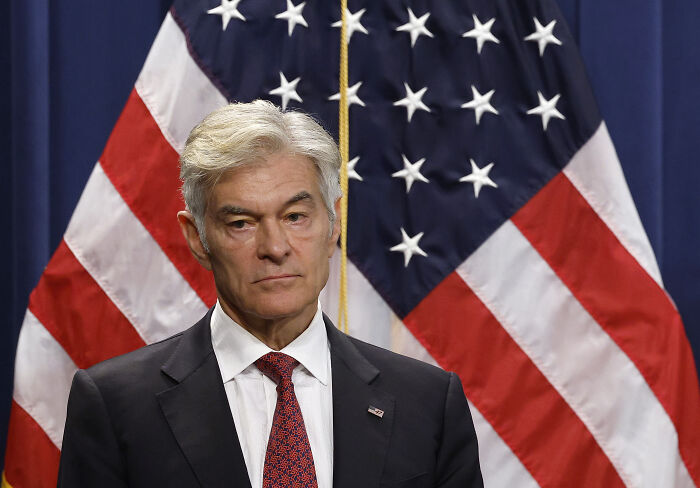 Dr. Oz standing in front of American flags, addressing federal workers after government shutdown during holiday season.