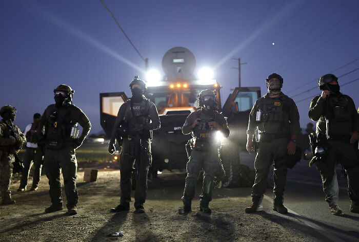 Heavily armed police officers stand in front of armored vehicle during Trump&rsquo;s ICE raids showing arrested but not convicted criminals.