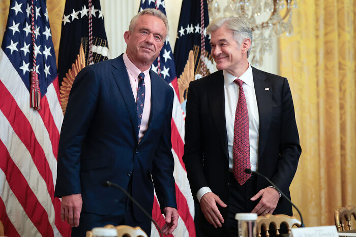 Two men in suits stand before American flags during a government event after brutal government shutdown advice.