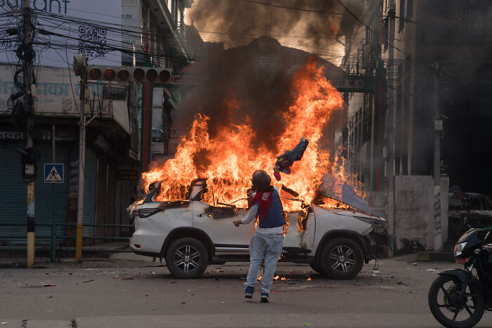 Person standing near a burning car amid chaos, representing one of the major events that shook the world in 2025.