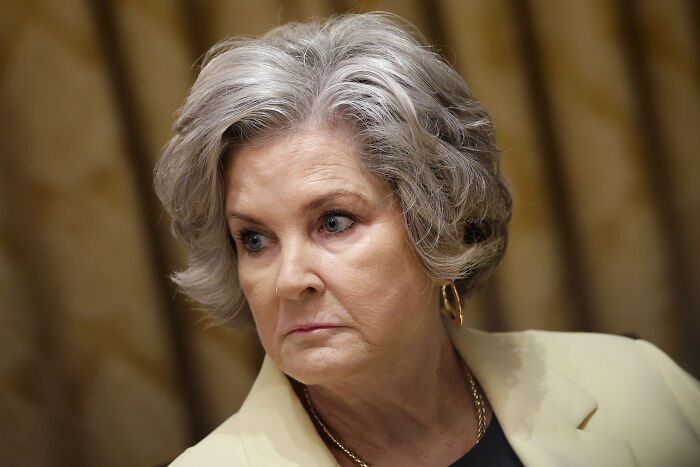 Woman with short gray hair and gold hoop earrings looking sideways, related to Trump&rsquo;s chief of staff and alcoholic personality claims.