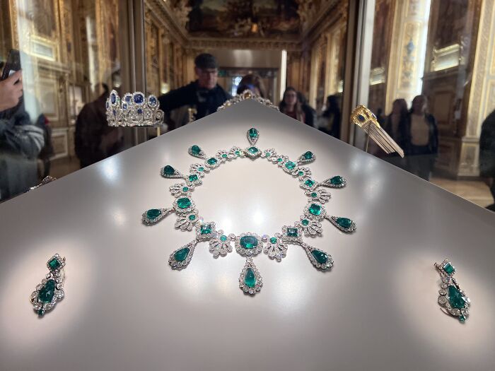 Emerald and diamond jewelry displayed in a museum with visitors observing the exhibits highlighting events that shook the world.