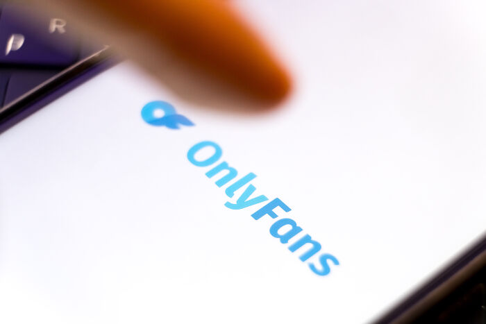 Close-up of a finger pointing to OnlyFans logo on a smartphone screen related to IRS agents reviewing x-rated content claims.