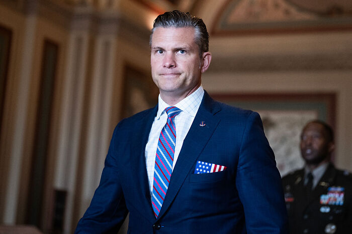 Man in a suit with an American flag pocket square, implicated in Trump throwing Hegseth under the bus over war crime scandal.