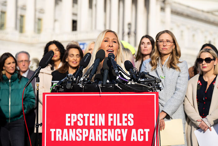MTG speaking at Epstein Files Transparency Act event with multiple microphones and supporters behind her outdoors.
