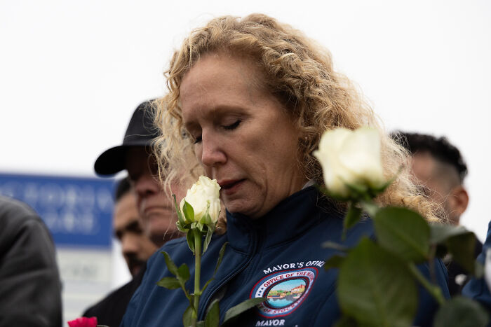 Woman holding white roses, mourning victims as manhunt continues for California gunman after children pass away.