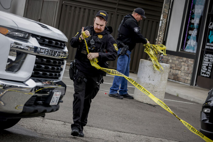 Two police officers setting up yellow caution tape at a California crime scene during manhunt for gunman.