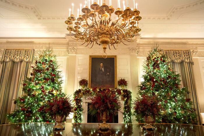 Elegant Christmas decorations with lush greenery and red accents in a grand room for Melania Trump&rsquo;s 2025 holiday display.