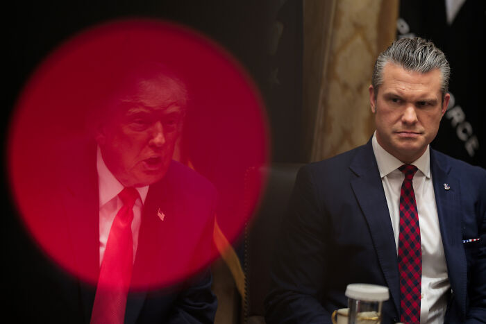 Donald Trump is seen through a red filter during an intense meeting, highlighting the authoritarian post controversy online.