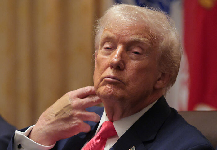 Donald Trump in a suit and red tie, making a gesture, related to his authoritarian post sparking fierce reactions online.