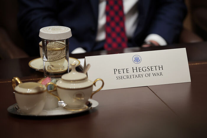 Nameplate for Pete Hegseth Secretary of War on a table during Trump&rsquo;s cabinet meeting with tea set and hourglass nearby.