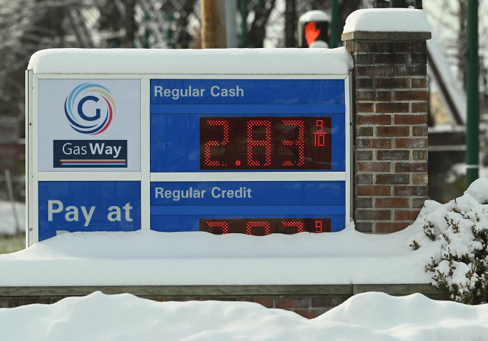 Gas station price sign covered in snow showing regular cash and credit rates during winter conditions.
