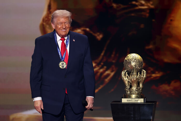Donald Trump wearing a medal standing next to a gold trophy, related to FIFA ethics complaint and Infantino peace prize.