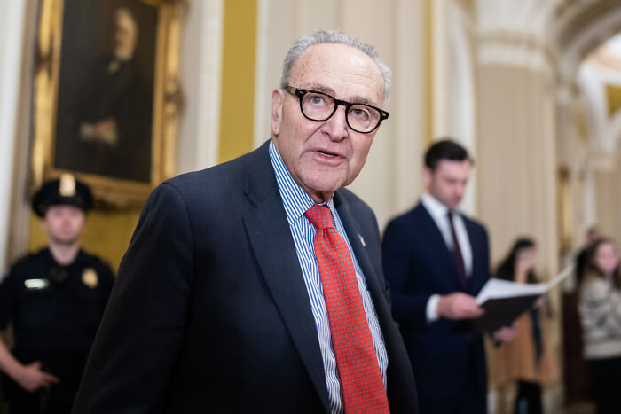 Man in glasses and red tie speaking indoors with uniformed officers and people in the background, relating to U.S. military d**g boat strikes.