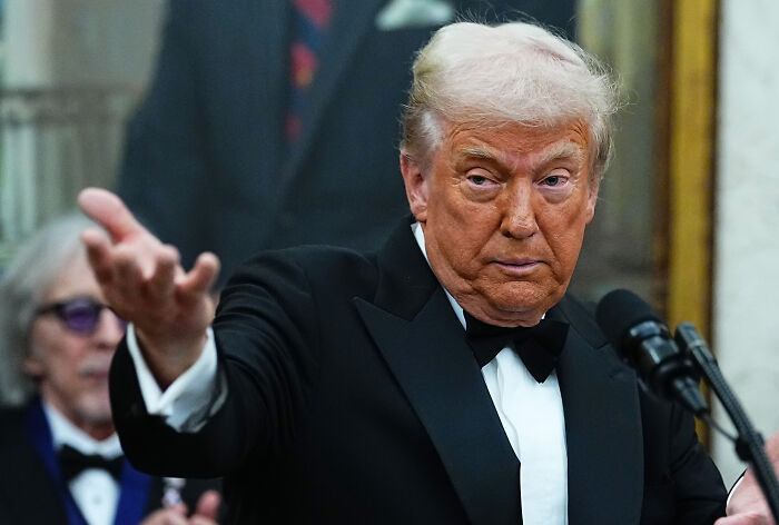 Former President Trump in a black tuxedo speaking at a podium during White House renovation updates amid his renovation spree.