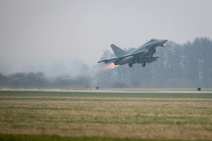 Military jet taking off with afterburner flame in a misty field, illustrating terrifying events closer to WW3.