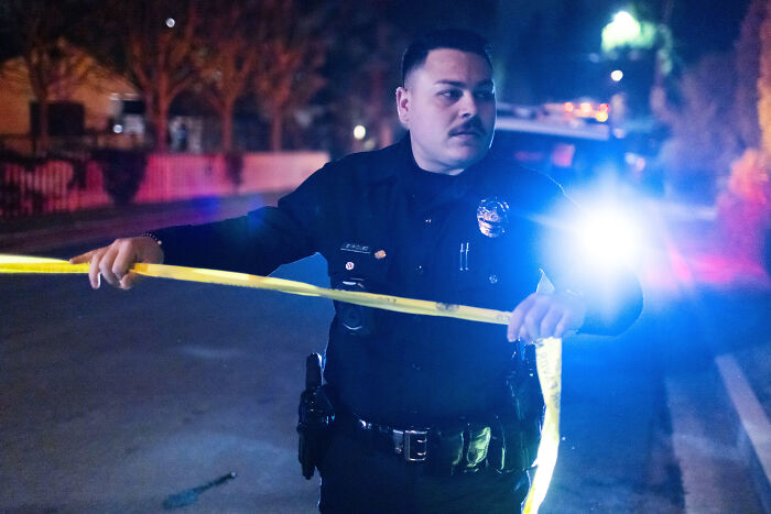Police officer managing a crime scene at night with caution tape, unrelated to Rob Reiner championing progressive causes.