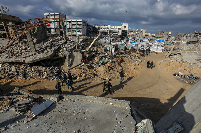 Ruins and rubble of buildings with people walking through the destruction, illustrating Trump gaslight claims and national impact.