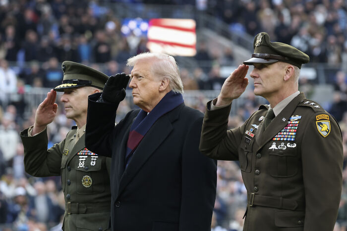 Donald Trump and military officials in uniform saluting during a public event amid war crimes criticism in the Caribbean.