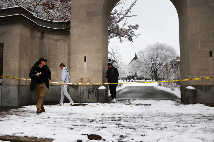 Snow-covered archway cordoned off with yellow tape as people walk nearby, reflecting tightened gun laws debate.