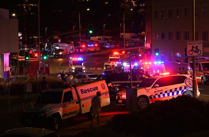 Police and rescue vehicles with flashing lights gather at night near Bondi Beach after an alleged gunman incident during Hanukkah.