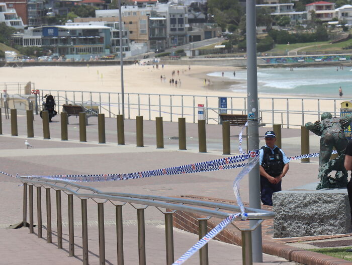 Police officer stands near taped-off area at Australian beach promenade amid tightened gun laws after mass shooting debate.