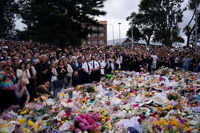 Large crowd gathered at a public memorial laying flowers reflecting on Australia's gun laws after first mass shooting in 30 years.