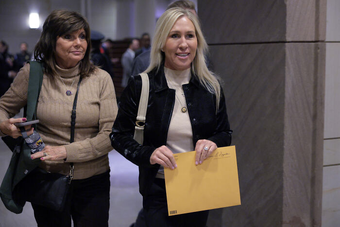 Marjorie Taylor Greene walking indoors holding an envelope while discussing Trump shouted my friends will get hurt claims.