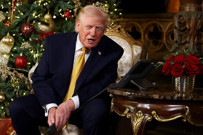 Donald Trump sitting by a decorated Christmas tree showing discoloration on his left hand during a White House call.