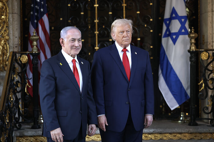 Donald Trump and another man in suits standing in front of U.S. and Israeli flags during a formal event about Venezuela.