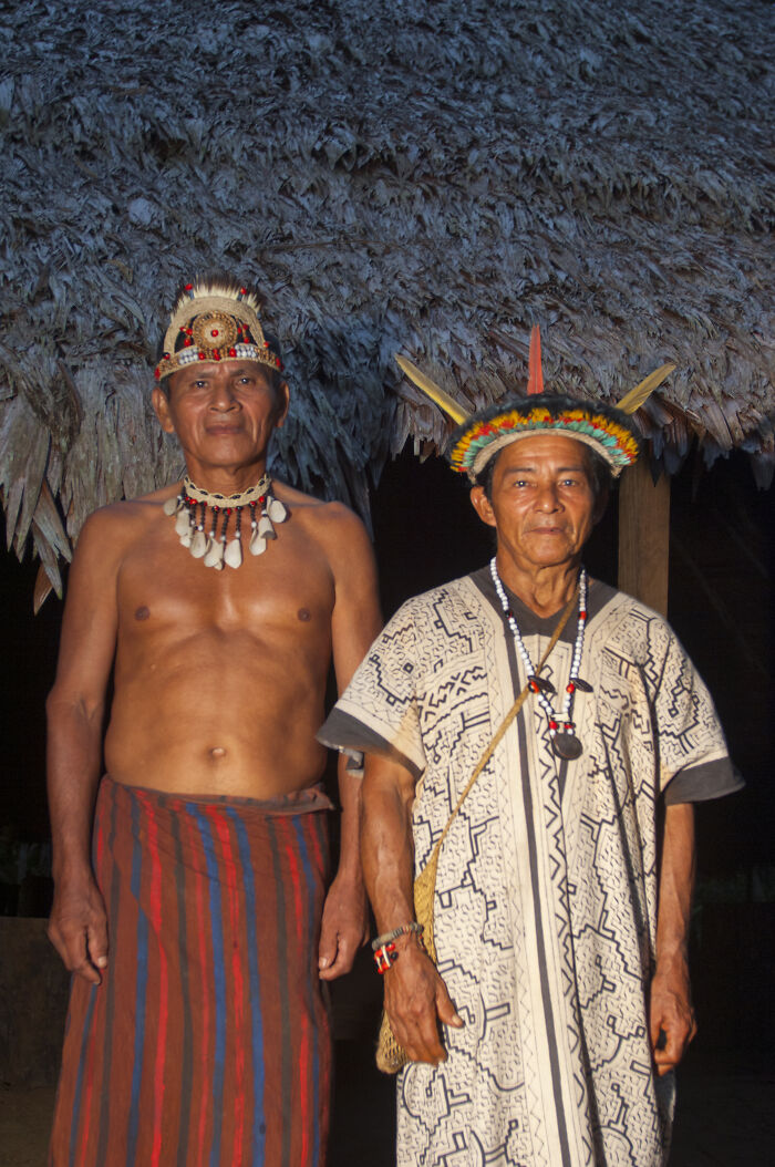 Two shamans in traditional attire standing against a thatched roof background, symbolizing a grim health forecast.