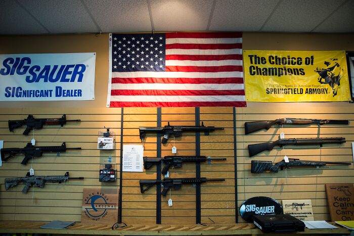 Firearms displayed on a wall under an American flag in a gun store highlighting Australia tightens gun laws debate.