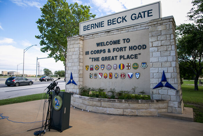 Entrance sign for Fort Hood with a podium of microphones, related to army gynecologist accused of secretly recording patients during exams