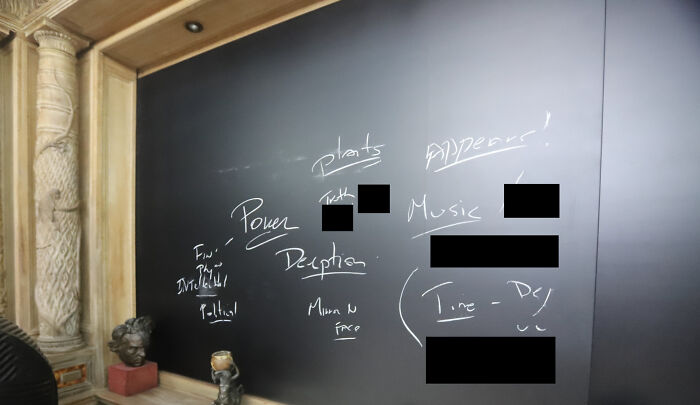 Chalkboard with notes on power, deception, and music inside a historic room, linked to Epstein bank records and island photos.