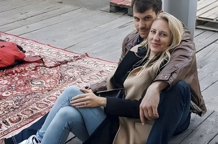 Young couple sitting together on wooden floor with a rug nearby, related to husband charged in disturbing case involving Miss Switzerland finalist wife