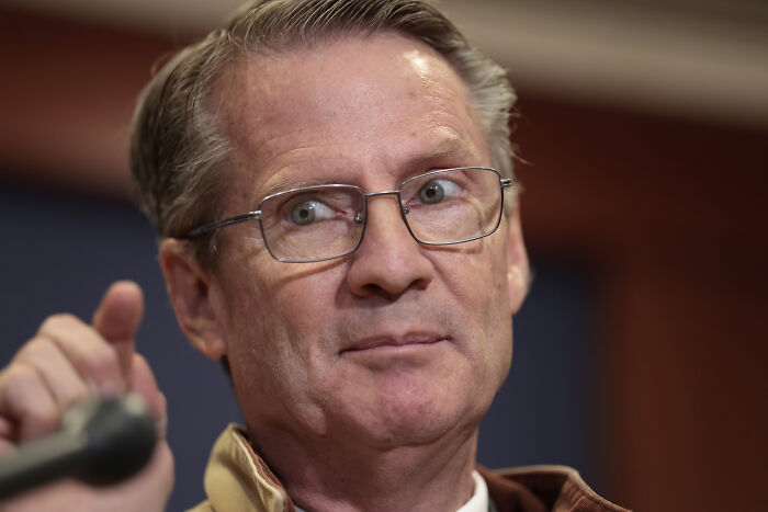 Man wearing glasses speaking at a microphone, related to Jack White slamming lawmaker over AI video controversy.