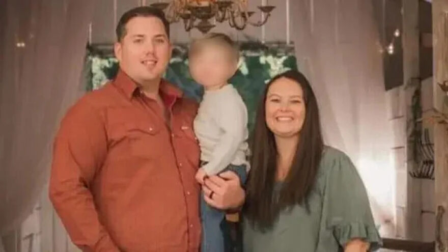 Man and woman standing indoors with toddler, representing deceased parents who were brutally attacked found with toddler cuddling.