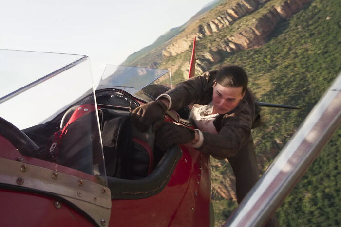 Tom Cruise hanging on outside a red plane over cliffs, showcasing a thrilling scene from his epic space movie.