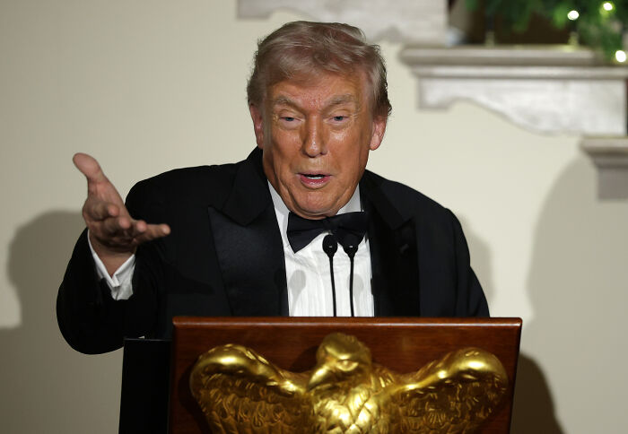 Donald Trump in a black tuxedo speaking at a podium with a golden eagle, sending unnerving signals about future plans.